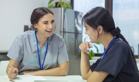 Two yoiung women in scrubs talk and laugh