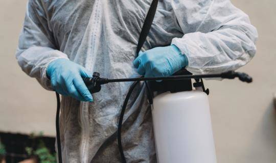 Person wearing coveralls and holding insecticide sprayer