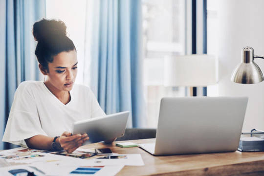 Woman studying her business's finances on a tablet and laptop