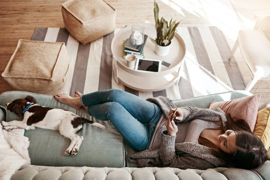 Woman looking at her phone while on the couch with her dog