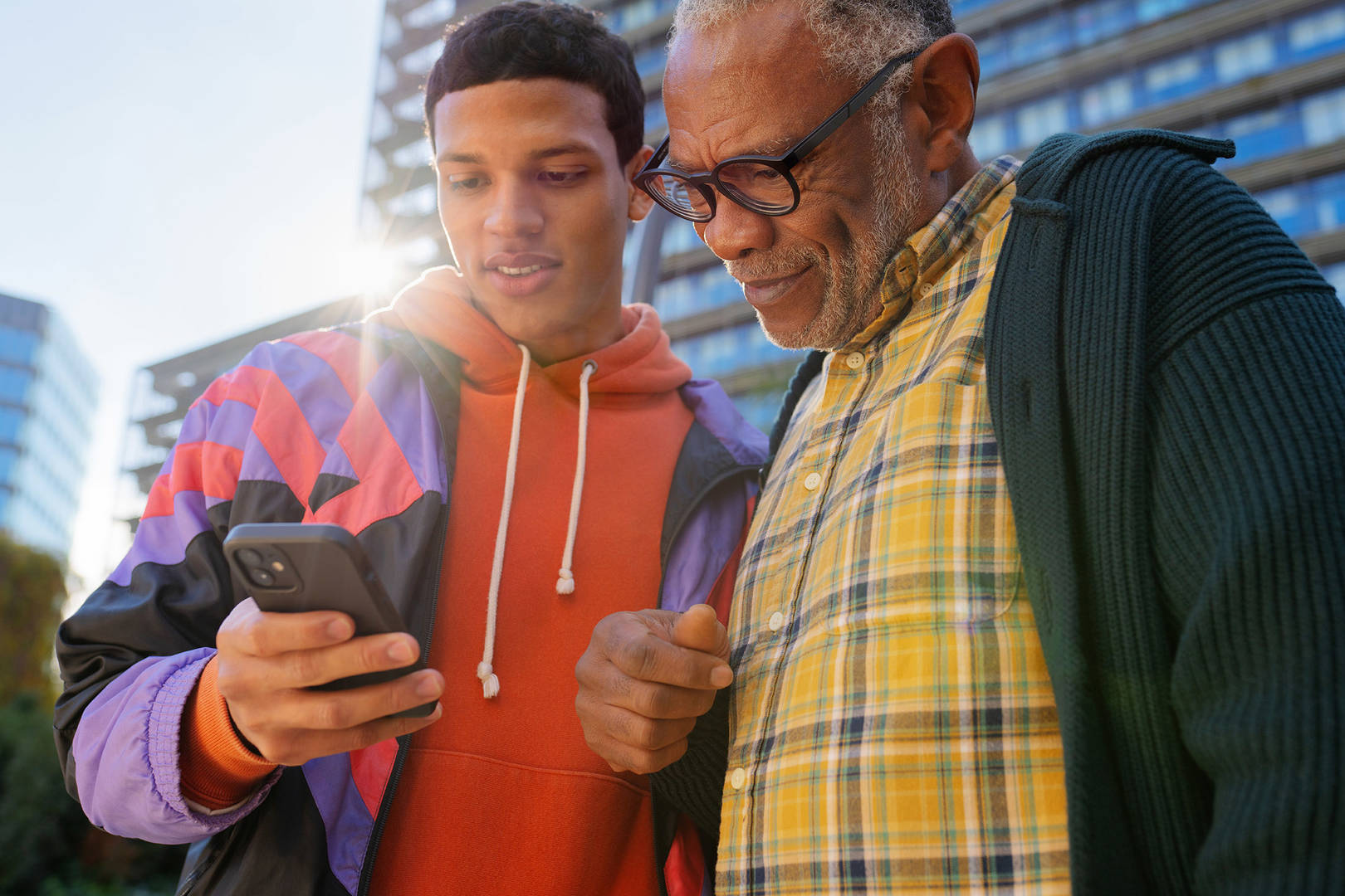 Casual portrait of a young man showing an older man something on his phone, shot on a sunny day in the city